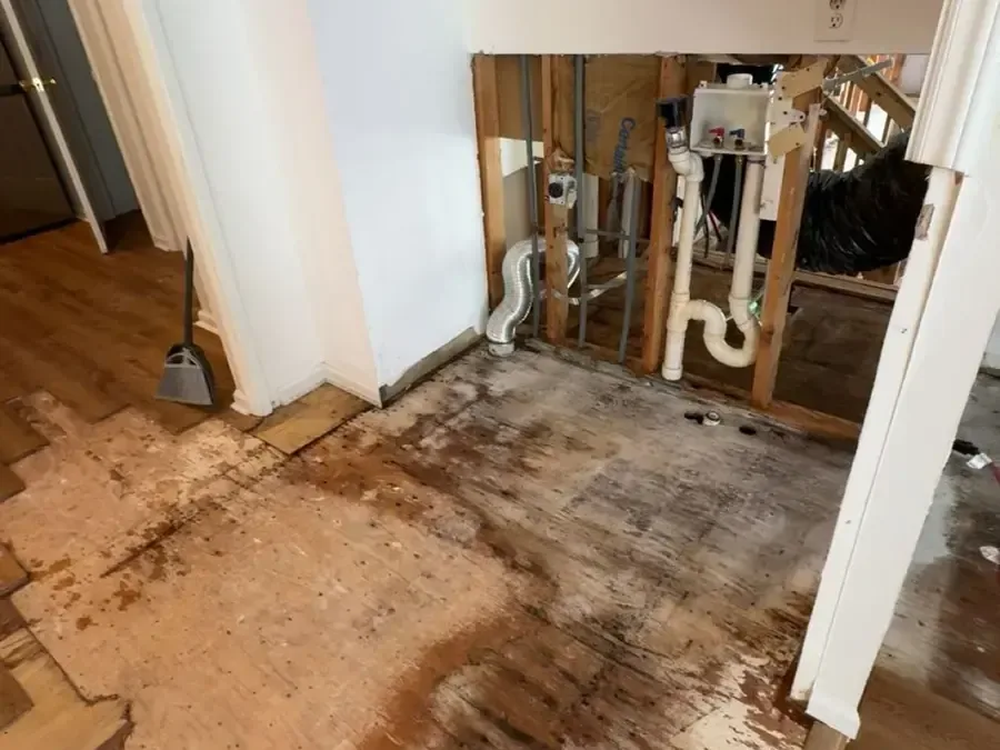 Opened plumbing wall beside flooring removed after a pipe leak