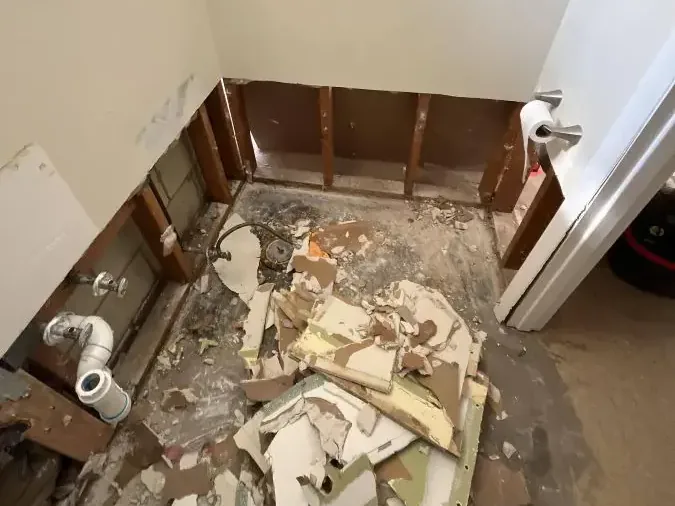 Exposed bathroom studs with broken material scattered on the floor